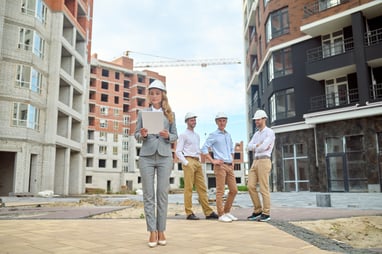 examination-serious-young-adult-woman-business-gray-suit-heels-wearing-safety-helmet-looking-document-smiling-three-men-waiting-construction-site